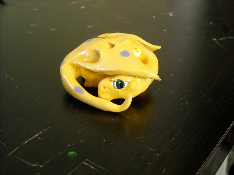 A small curled up yellow glazed dragon with purple polkadots