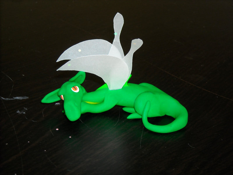 A green polymer dragon lying down, with paper wings
